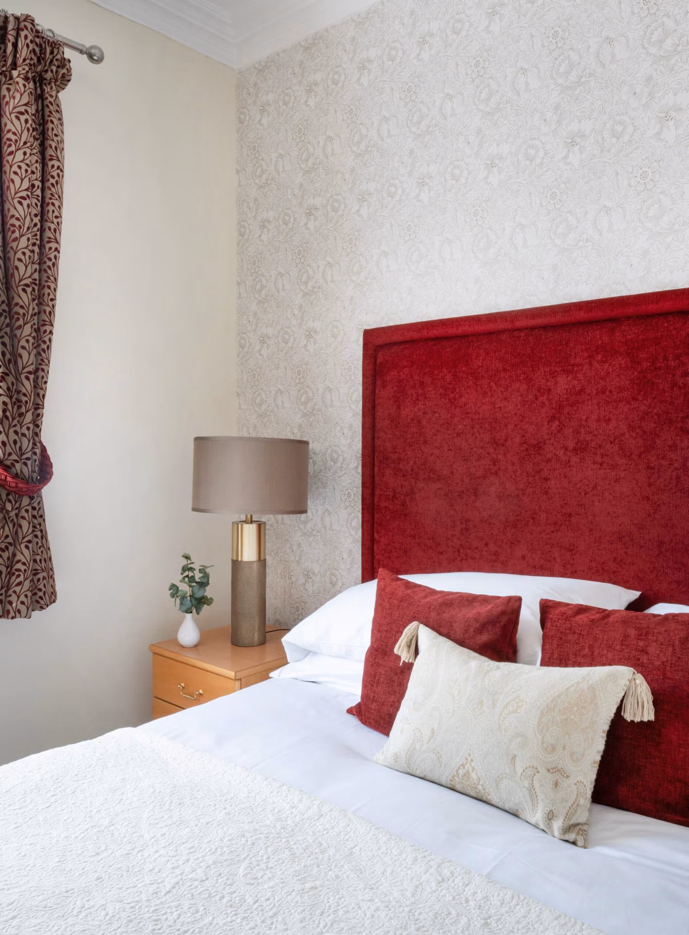 A bed with a red headboard, pillows and fresh white sheets