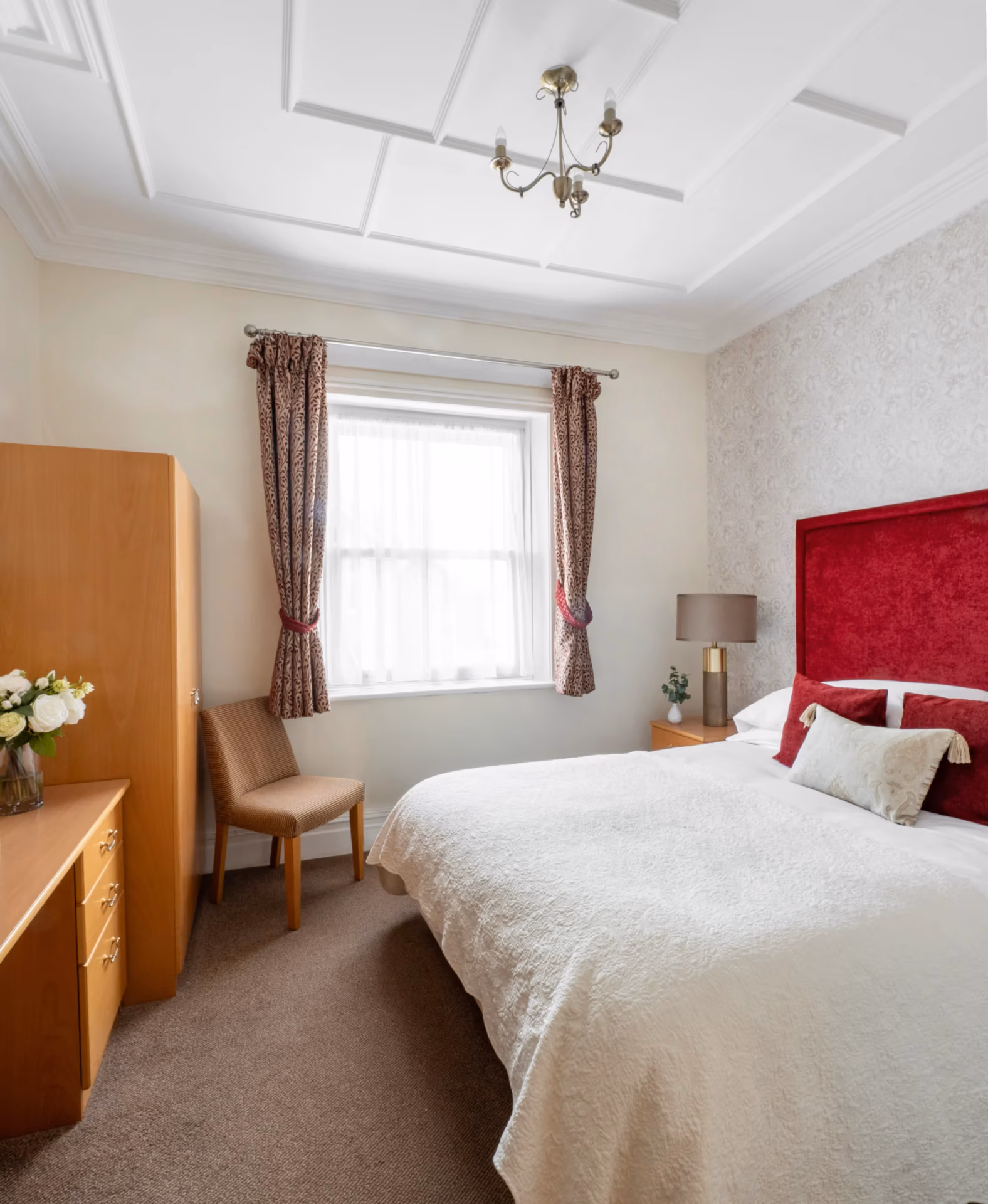 A large bed with a red headboard in a room with a chair and desk