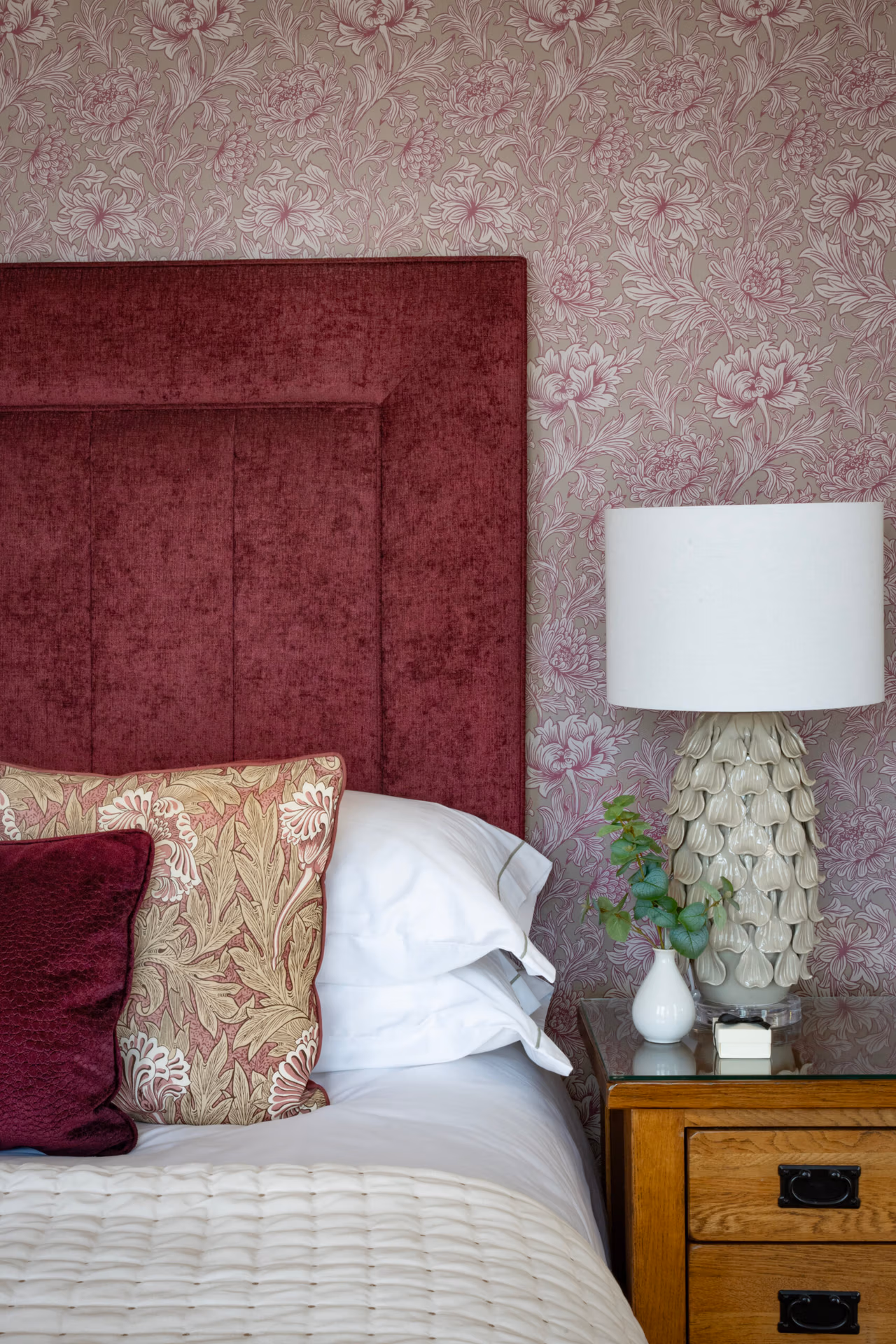 A burgundy headboard, bedside table, lamp and plant